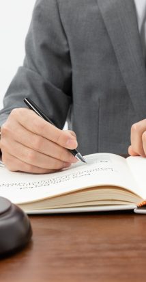 closeup-shot-of-person-writing-in-book-with-gavel-on-the-table
