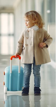 Child at the airport. Little girl with a suitcase. Girl in brown coat.